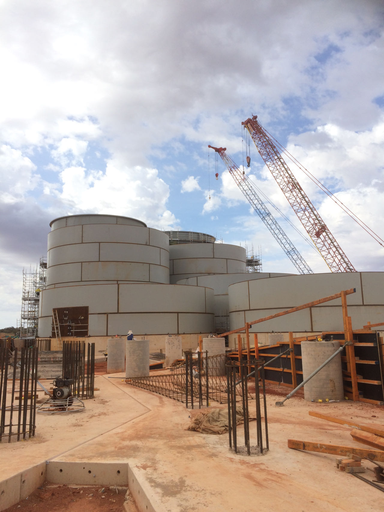 Large fabricated tanks under construction with crawler cranes on site